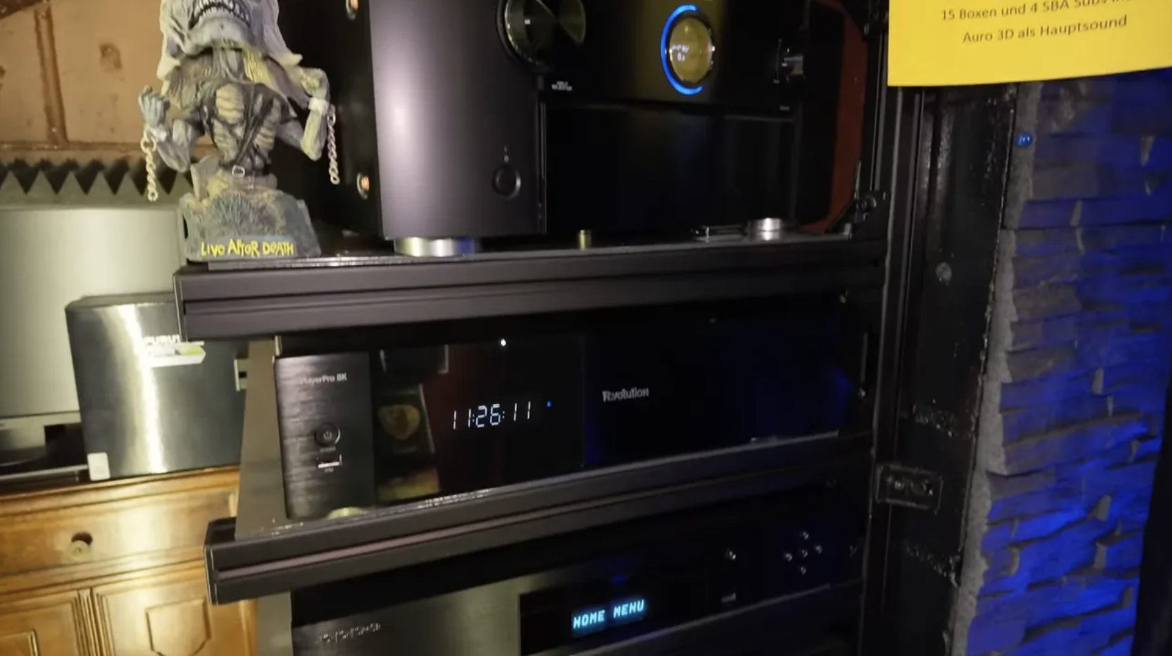 Technikrack mit mehreren schwarzen Geräten hinter einem Vorhang im Nebenraum